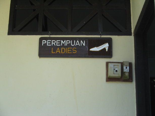 壁に掛けられた案内看板。「PEREMPUAN」「LADIES」と書かれ、右側にハイヒールのイラストが描かれている。