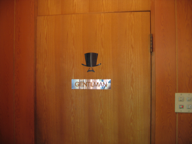 ドアに貼られた案内表示。黒いシルクハット・鼻・口ひげのイラストの下に、「GENTLMAN」(原文ママ)と書かれている。