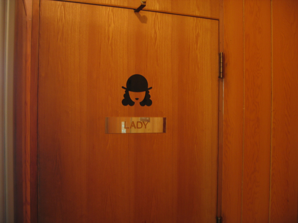 ドアに貼られた案内表示。黒い帽子・髪・唇を描いたイラストの下に「LADY」と書かれている。